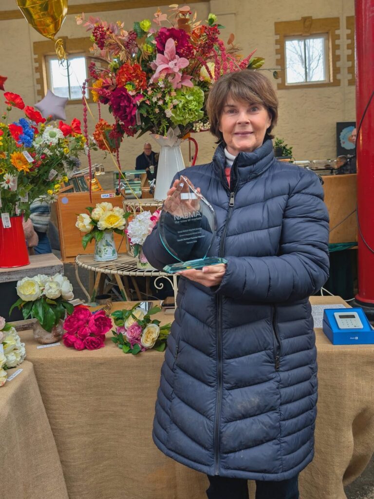 A flower trader holding the Britain’s Favourite Market trophy at her stall