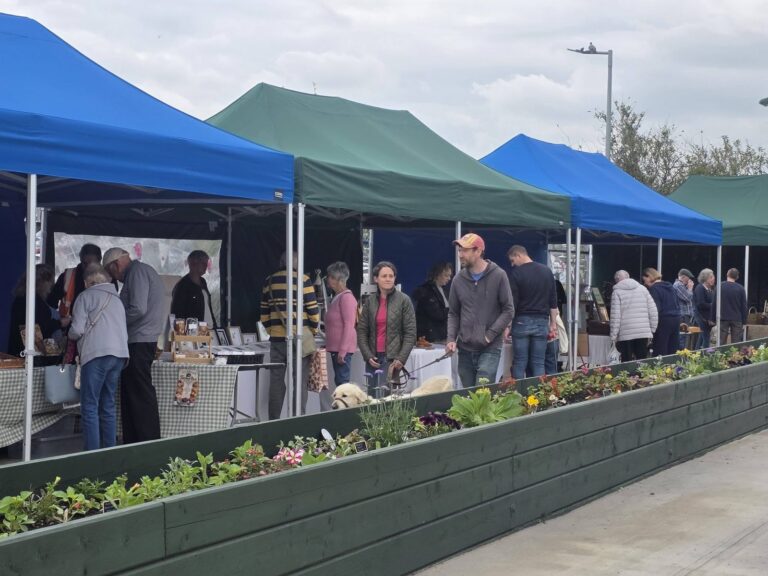 Customers browsing blue and green gazebo stalls beside the planters in Drovers Yard