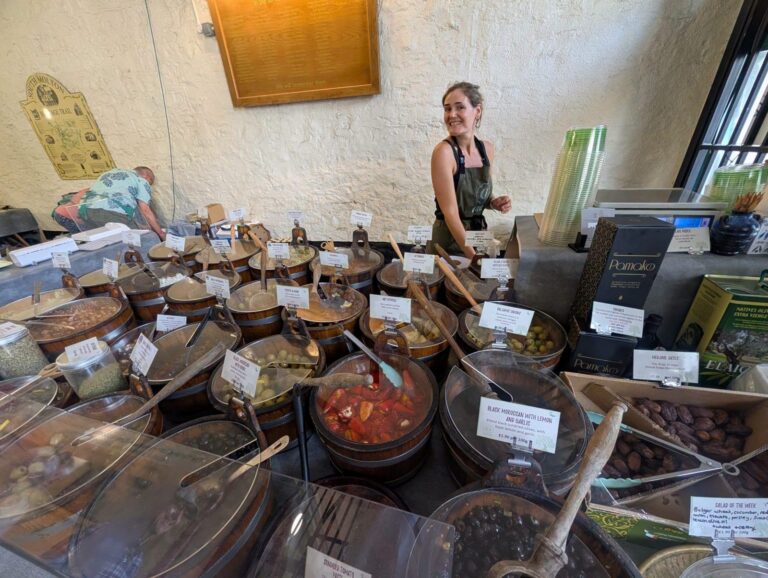 A trader behind a display of olives and deli foods